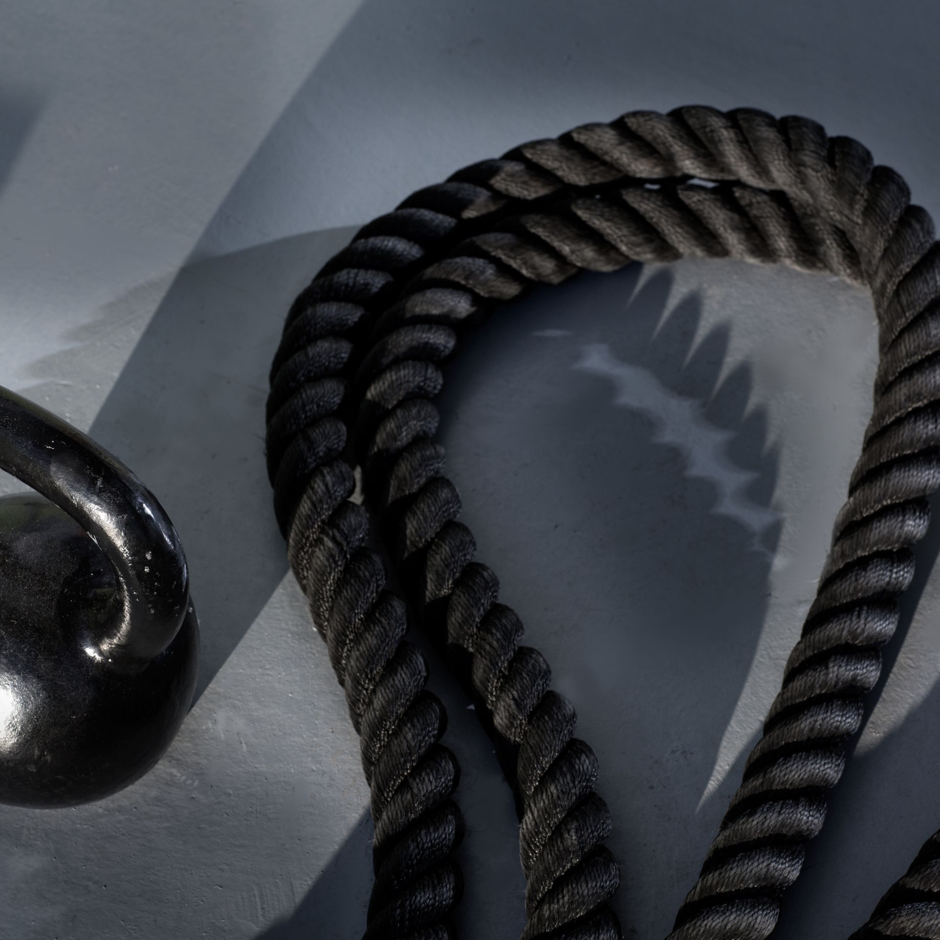 Close-up of a heavy black kettlebell and a thick coiled rope on a gray surface.